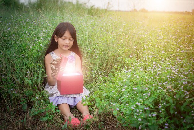 little girl sitting by the field with a gift and looking at it,