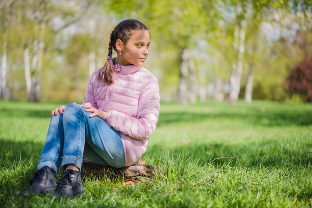 Маленькая девочка сидит, глядя в сторону в парке