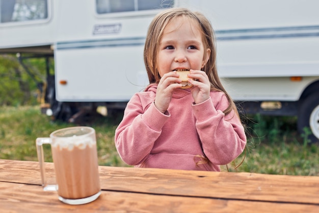 캠핑카 근처에 앉아서 쿠키와 구운 마시멜로로 만든 스모어를 먹는 어린 소녀