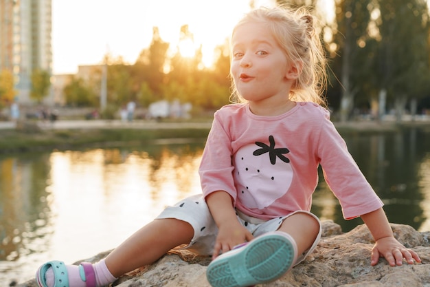 호수 근처 공원에 있는 거대한 돌 위에 앉아 있는 어린 소녀
