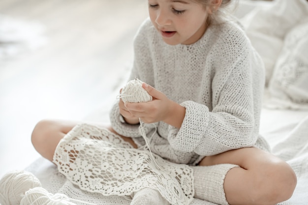 Little girl sitting on the sofa and learning to knit, home leisure concept.