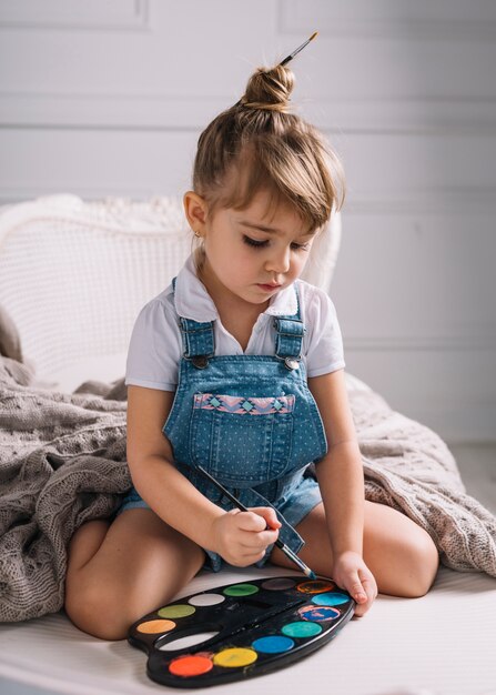 Little girl sitting on sofa with bright aquarelle palette