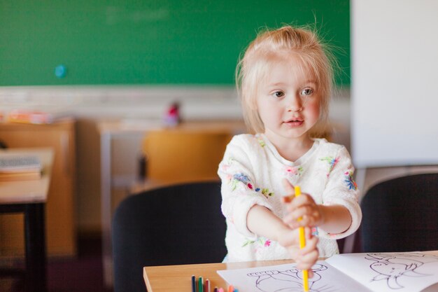 Маленькая девочка, сидя за столом в классе