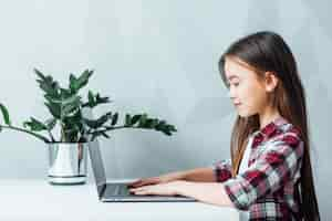 Free photo little girl sitting at table and using modern tablet