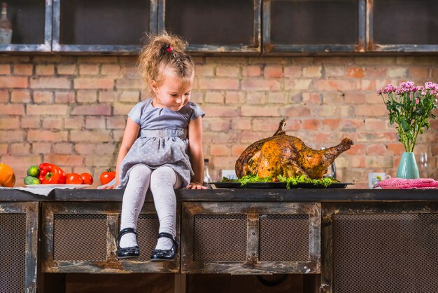 Little girl sitting on table with baked turkey