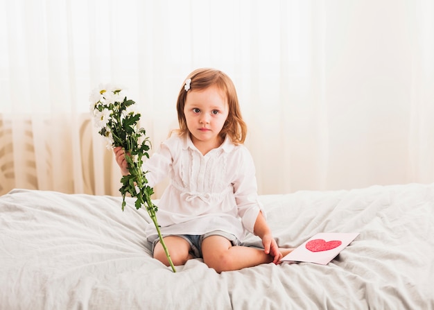 Little girl sitting with flowers and greeting card 