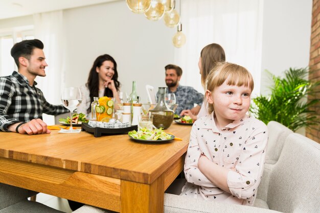 Little girl sitting with funny adults at table