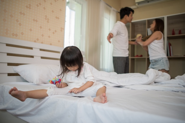 Little Girl sitting with her parents on the bed looking serious