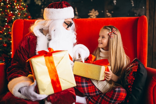 Free photo little girl sitting with santa and presents on christmas