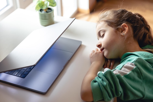 어린 소녀는 탁자 위의 노트북 앞에서 잔다
