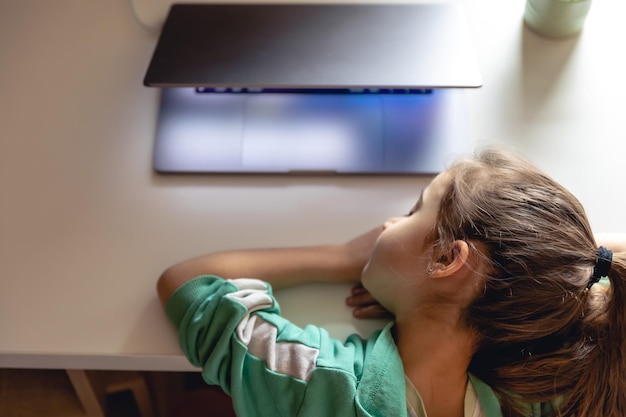 La bambina dorme davanti a un computer portatile sul tavolo