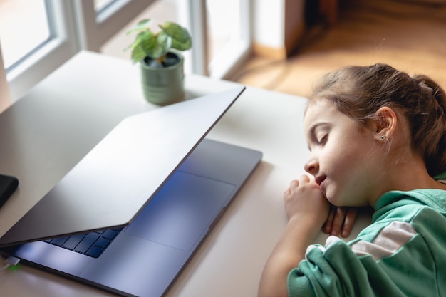 Little girl sleeps in front of a laptop on the table