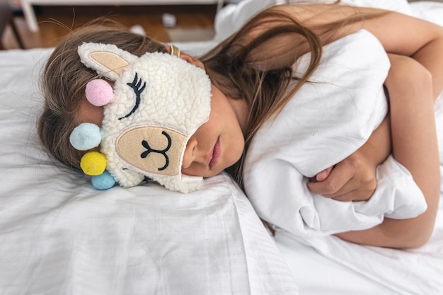 A little girl sleeps on a pillow wearing a funny sleep mask