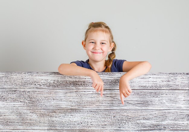 Little girl smiling and gesturing below in t-shirt , front view.