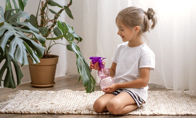 Little girl spraying houseplant leaves, taking care of plant Monstera.