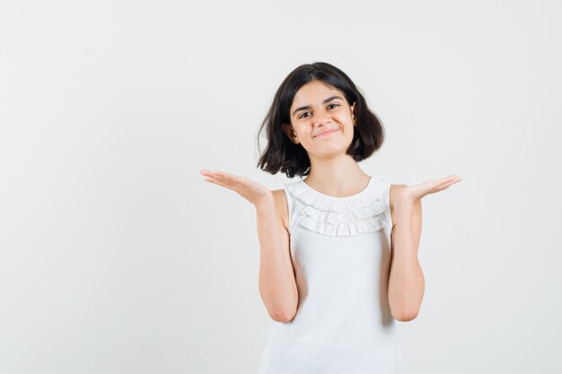 Little girl spreading palms as holding something in white blouse and looking jolly , front view.