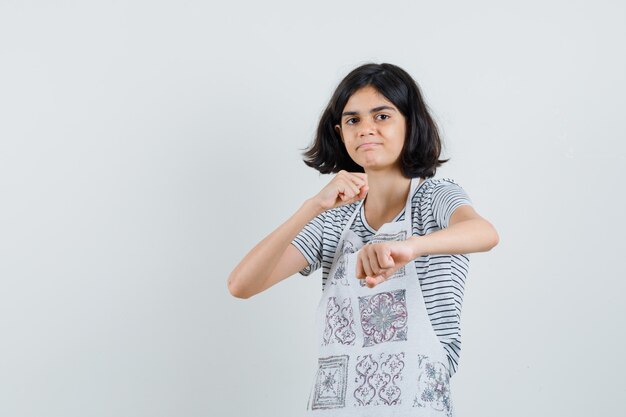 Little girl standing in fight pose in t-shirt, apron and looking confident