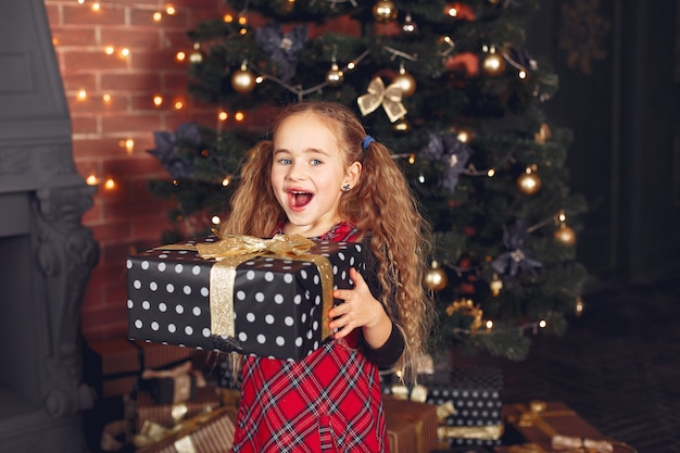 Little girl standing near christmas tree with present