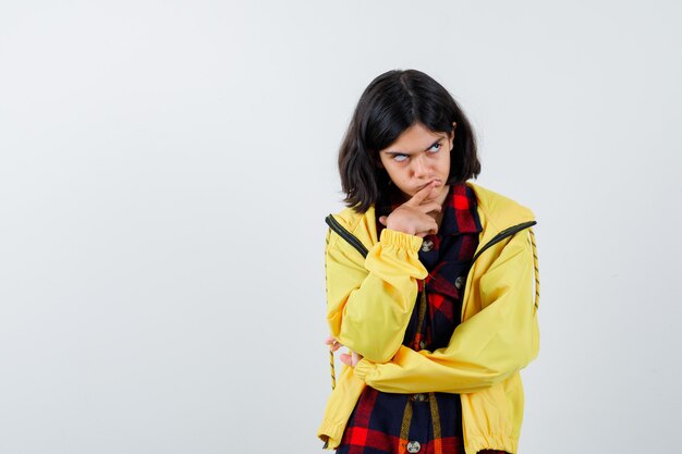 Little girl standing in thinking pose in checked shirt, jacket and looking hesitant