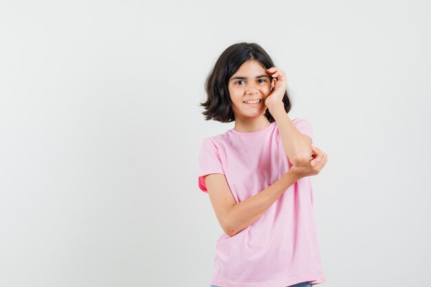 Little girl standing in thinking pose in pink t-shirt and looking glad , front view.