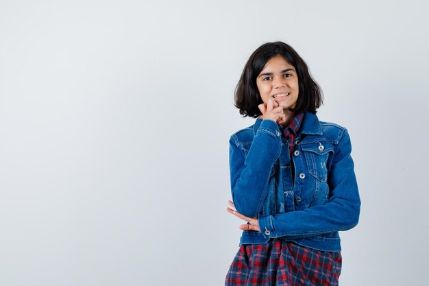 Little girl standing in thinking pose in shirt, jacket and looking cheerful. front view.