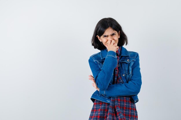 Little girl standing in thinking pose in shirt, jacket and looking mournful. front view.