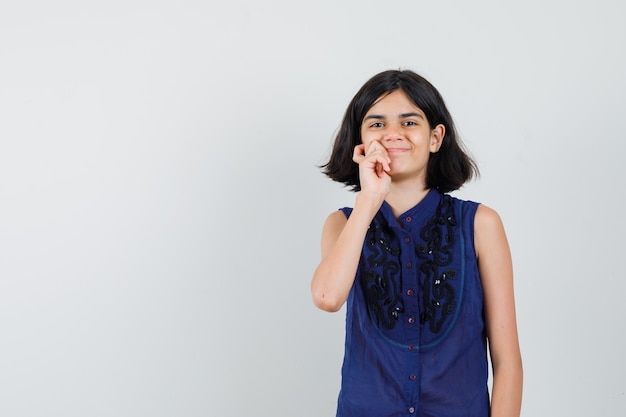 Bambina in piedi nella posa di pensiero e sorridente in camicetta blu