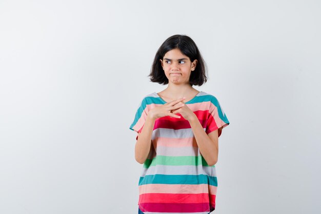 Free photo little girl standing in thinking pose in t-shirt and looking doubtful , front view.