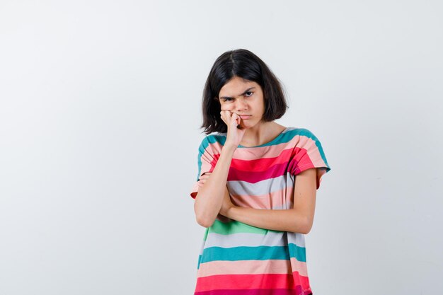 Little girl standing in thinking pose in t-shirt and looking pensive , front view.