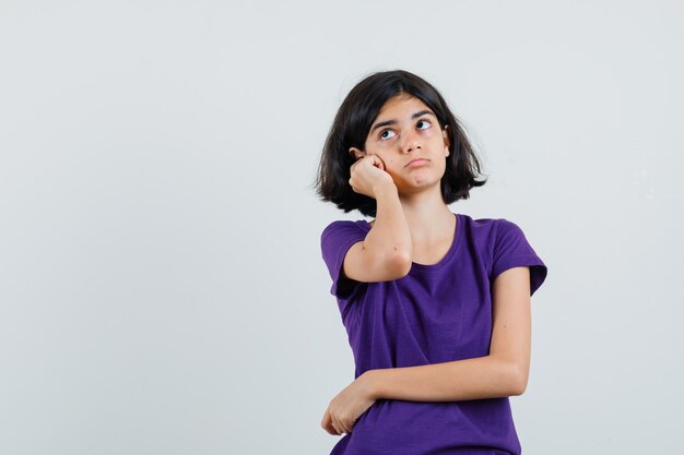 Little girl standing in thinking pose in t-shirt and looking puzzled.