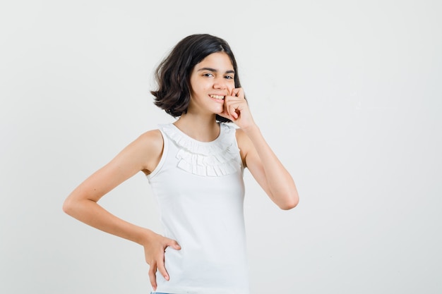 Little girl standing in thinking pose in white blouse and looking jolly. front view.