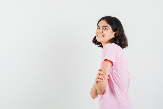 Little girl standing with crossed arms in pink t-shirt and looking cheerful. .