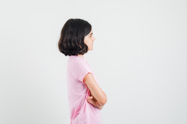 Little girl standing with crossed arms in pink t-shirt and looking focused .