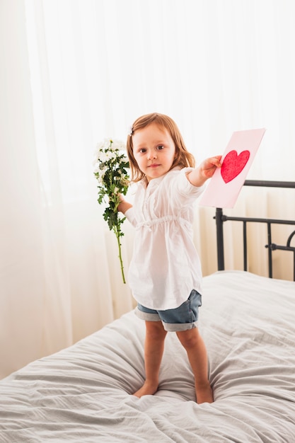 Little girl standing with flowers and greeting card 