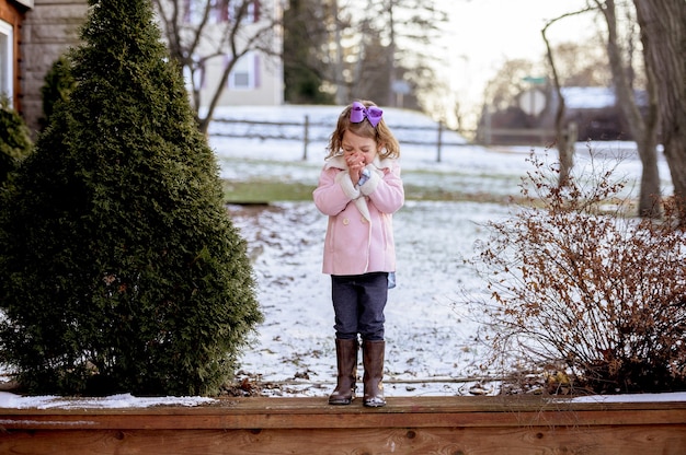 雪に覆われた庭で木の板の上に立って、日光の下で祈る少女