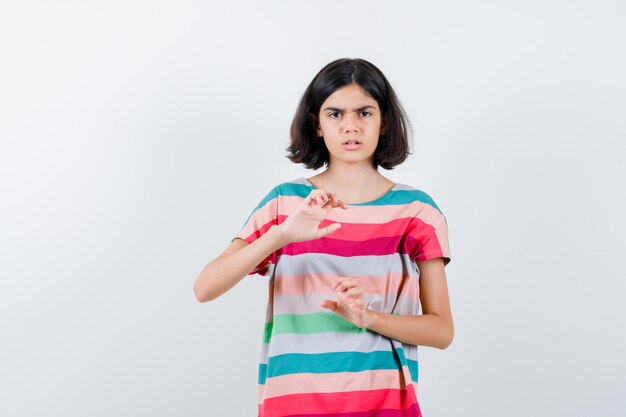 Little girl stretching hands as holding something in t-shirt and looking angry , front view.