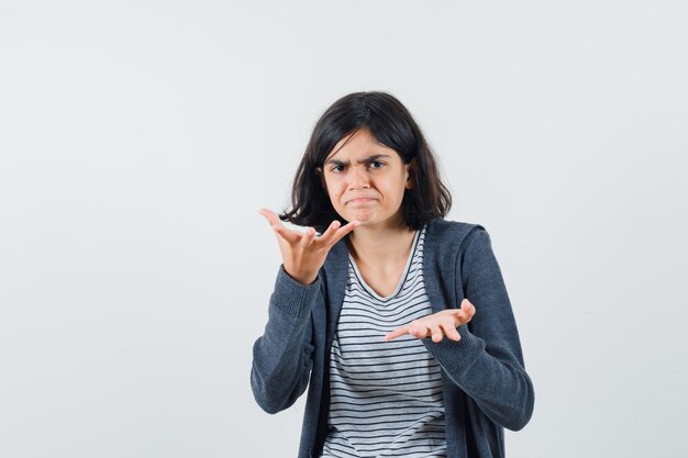 Little girl stretching hands in questioning gesture in t-shirt, jacket and looking puzzled