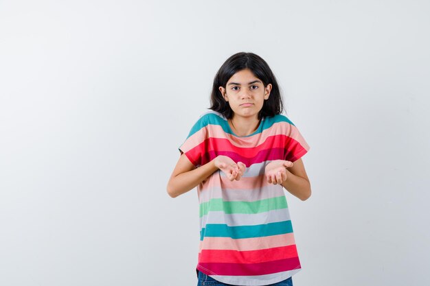 어린 소녀는 티셔츠를 입고 질문하는 방식으로 손을 뻗고 어리둥절해 보입니다. 전면보기.