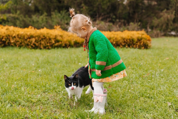 Маленькая девочка гладит черную кошку в парке. девушка гладит кошку. дети и животные.