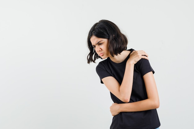 Little girl suffering from shoulder pain in black t-shirt and looking fatigued , front view.