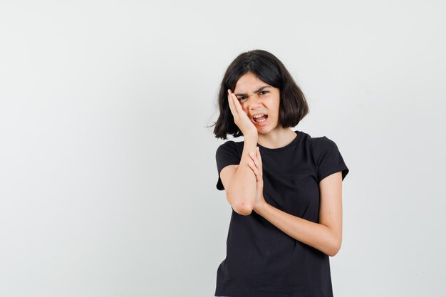 Little girl suffering from toothache in black t-shirt and looking annoyed. front view.