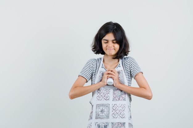 Little girl in t-shirt, apron holding bottle of pills and looking peaceful ,