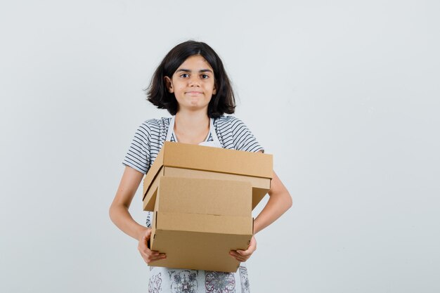 Little girl in t-shirt, apron holding cardboard boxes ,