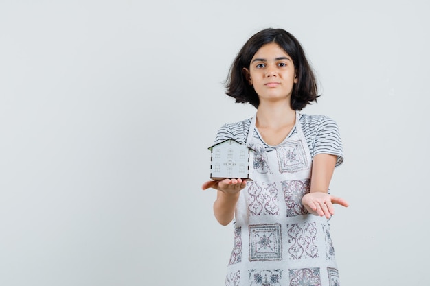 Little girl in t-shirt, apron presenting house model and looking confident ,