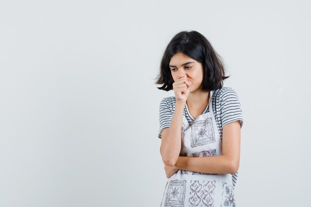 Little girl in t-shirt, apron suffering from cough and looking upset ,