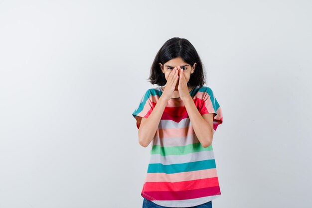 Little girl in t-shirt covering nose and mouth with hands and looking excited , front view.