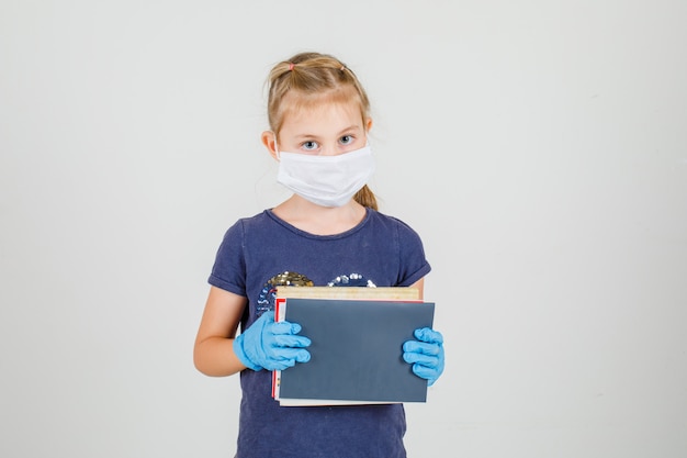 Tシャツ、手袋、本やノートを押しながら注意深く、正面を見て医療マスクの少女。