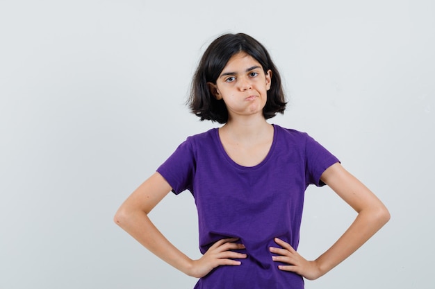 Free photo little girl in t-shirt holding hands on waist and looking confused ,