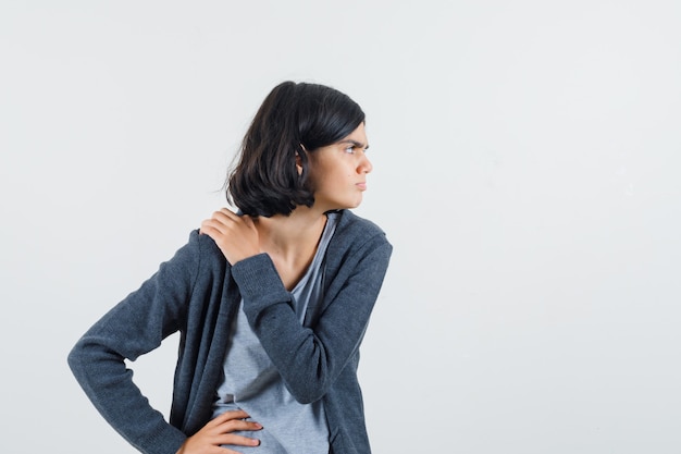 Little girl in t-shirt, jacket holding hand on shoulder and looking focused