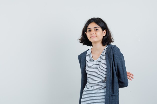 Little girl in t-shirt, jacket holding hands behind back and looking confident ,